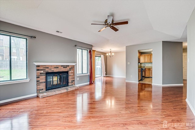 unfurnished living room featuring visible vents, a brick fireplace, baseboards, ceiling fan with notable chandelier, and light wood-style floors