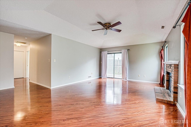 unfurnished living room with a ceiling fan, a textured ceiling, a brick fireplace, light wood-type flooring, and lofted ceiling