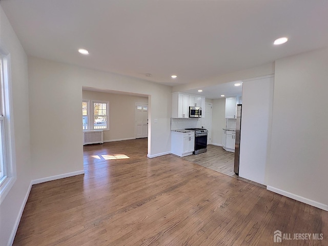 kitchen with light wood-type flooring, backsplash, stainless steel appliances, white cabinets, and radiator heating unit