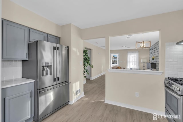 kitchen with light wood finished floors, appliances with stainless steel finishes, a notable chandelier, and gray cabinetry