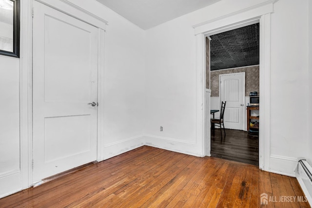 empty room featuring baseboard heating and wood-type flooring