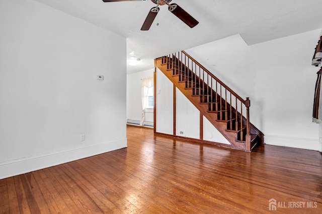 unfurnished living room with stairway, ceiling fan, wood-type flooring, and a baseboard radiator