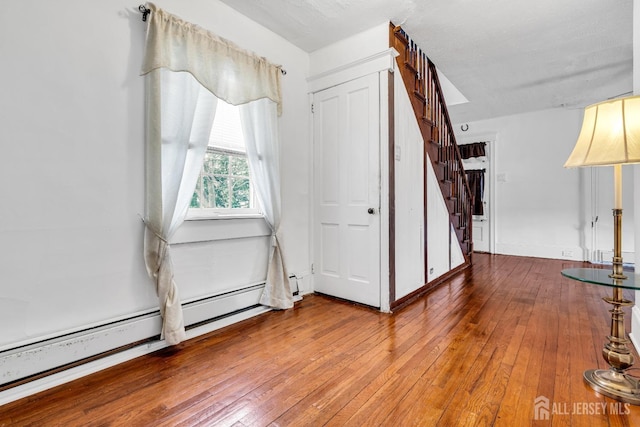 foyer featuring a baseboard heating unit, stairway, and wood-type flooring