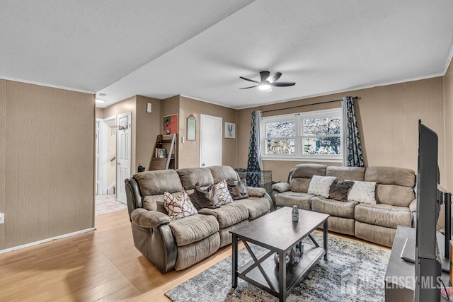 living room with ceiling fan, a textured ceiling, crown molding, light wood-type flooring, and baseboards