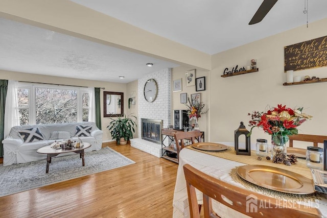 living room with light wood-type flooring, a brick fireplace, ceiling fan, and baseboards