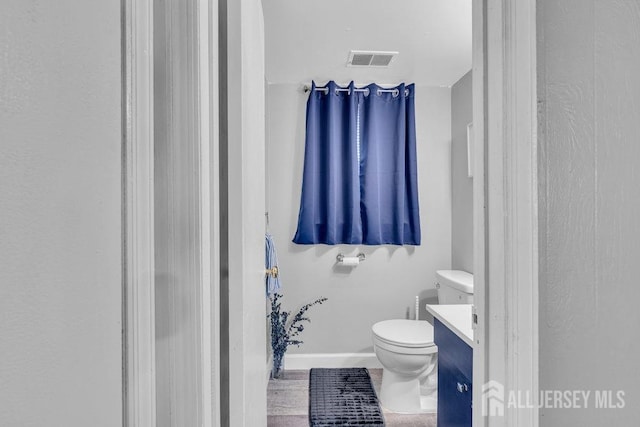 half bathroom with toilet, baseboards, visible vents, and vanity