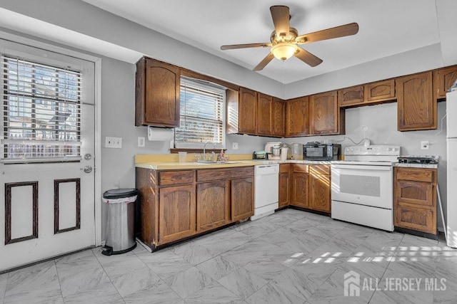 kitchen featuring brown cabinets, ceiling fan, a sink, white appliances, and light countertops