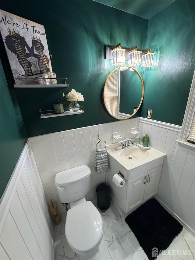 bathroom featuring vanity, wainscoting, toilet, and marble finish floor
