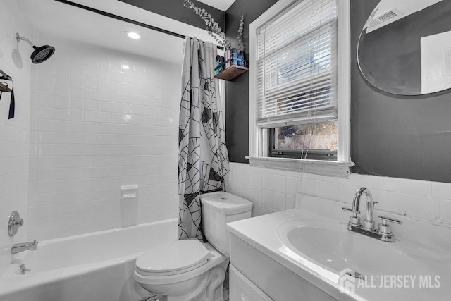 full bathroom featuring vanity, toilet, tile walls, shower / bathtub combination with curtain, and a wainscoted wall