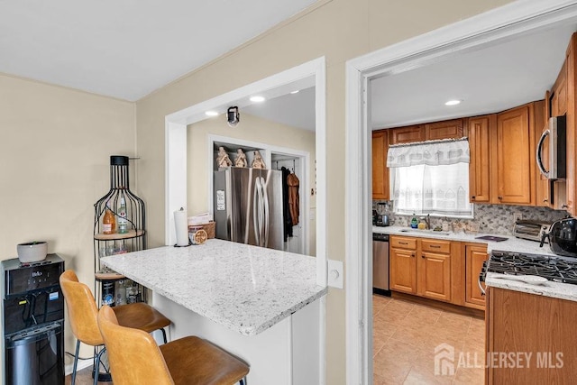 kitchen with a breakfast bar, brown cabinets, decorative backsplash, appliances with stainless steel finishes, and a sink