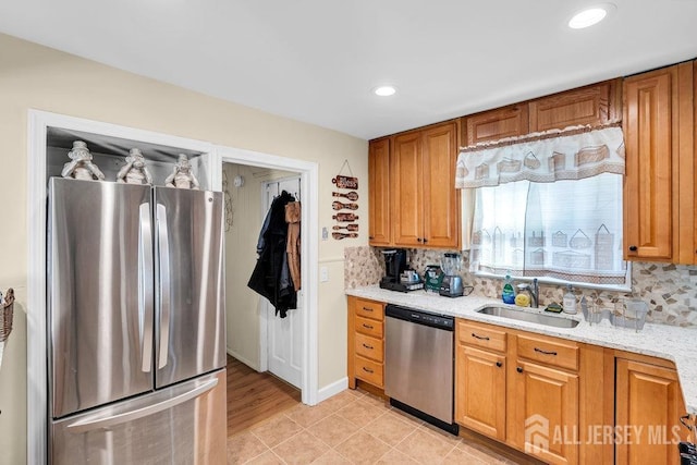 kitchen with appliances with stainless steel finishes, backsplash, a sink, and light stone counters