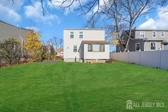 rear view of property featuring a lawn and fence