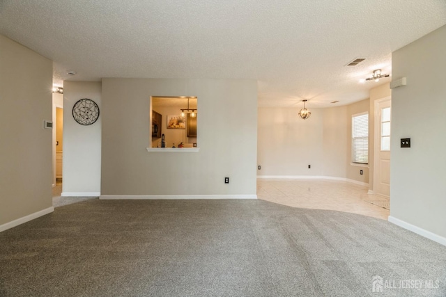unfurnished room featuring carpet floors, visible vents, a textured ceiling, and a chandelier
