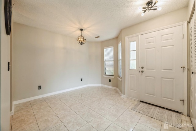 foyer entrance featuring an inviting chandelier, a textured ceiling, baseboards, and light tile patterned flooring