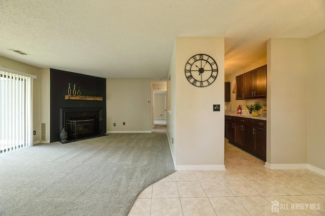 unfurnished living room with a textured ceiling, visible vents, a fireplace with flush hearth, light tile patterned floors, and baseboards