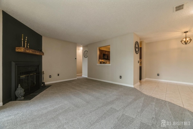 unfurnished living room with visible vents, baseboards, a textured ceiling, a fireplace with flush hearth, and carpet