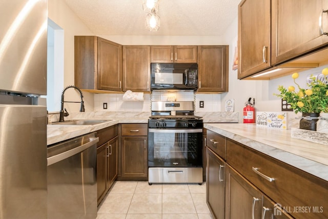kitchen with decorative backsplash, light tile patterned flooring, a textured ceiling, a sink, and stainless steel appliances