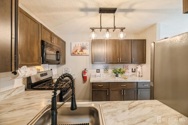 kitchen with a textured ceiling, decorative light fixtures, light countertops, a sink, and stainless steel appliances