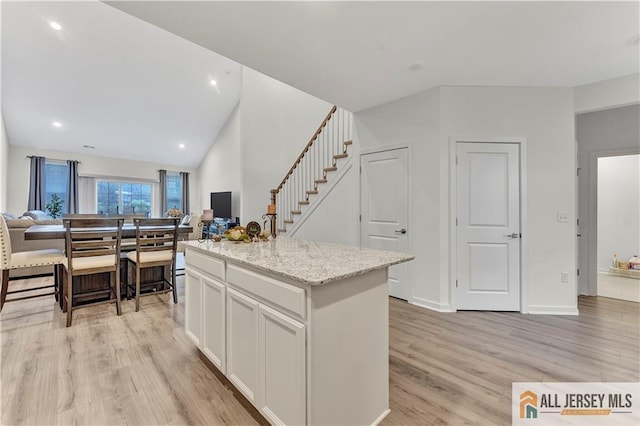 kitchen featuring light stone countertops, open floor plan, a center island, white cabinets, and light wood finished floors