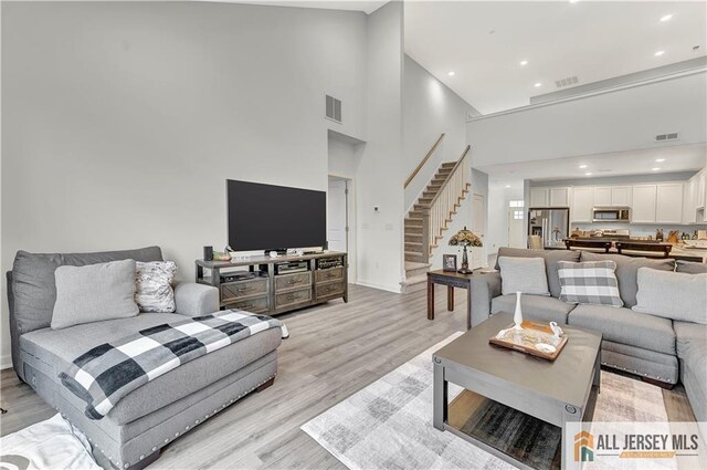 living room featuring a high ceiling, visible vents, stairway, and light wood-type flooring