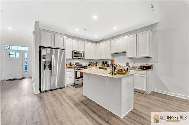 kitchen featuring light stone countertops, an island with sink, stainless steel appliances, baseboards, and light wood-type flooring