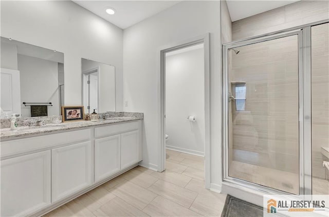 bathroom featuring double vanity, a shower stall, toilet, and a sink