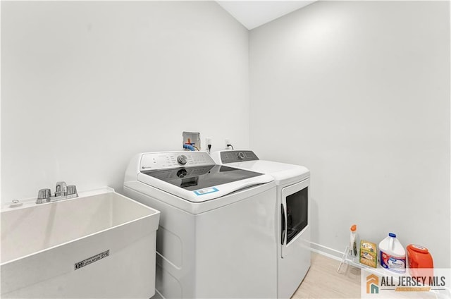 clothes washing area with laundry area, a sink, separate washer and dryer, baseboards, and light wood-type flooring