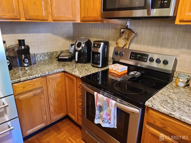 kitchen with parquet flooring, stainless steel appliances, light stone countertops, and backsplash