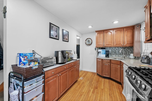 kitchen with light countertops, a sink, tasteful backsplash, light wood-style flooring, and stainless steel range with gas stovetop