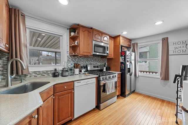 kitchen with light wood-type flooring, a sink, backsplash, stainless steel appliances, and baseboards