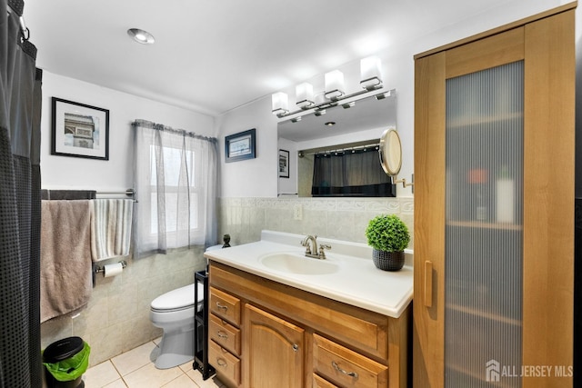 full bath featuring tile walls, toilet, tile patterned floors, vanity, and wainscoting