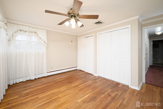 unfurnished bedroom featuring two closets, ornamental molding, baseboard heating, light wood-style floors, and a ceiling fan