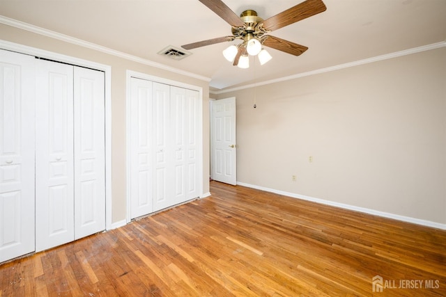 unfurnished bedroom featuring baseboards, visible vents, light wood-style floors, multiple closets, and crown molding