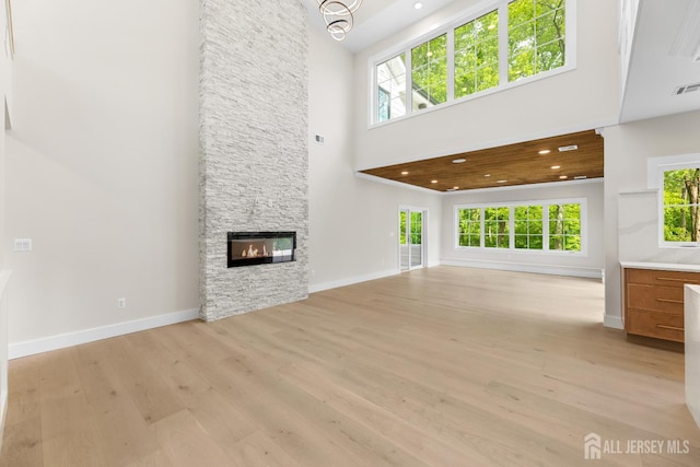 116 Hunt Dr, Princeton, NJ 08540 - unfurnished living room with a towering ceiling, light wood-style floors, a stone fireplace, baseboards, and a chandelier