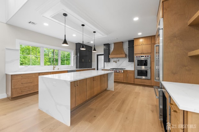 116 Hunt Dr, Princeton, NJ 08540 - kitchen featuring custom range hood, appliances with stainless steel finishes, light wood-style flooring, brown cabinets, and a large island