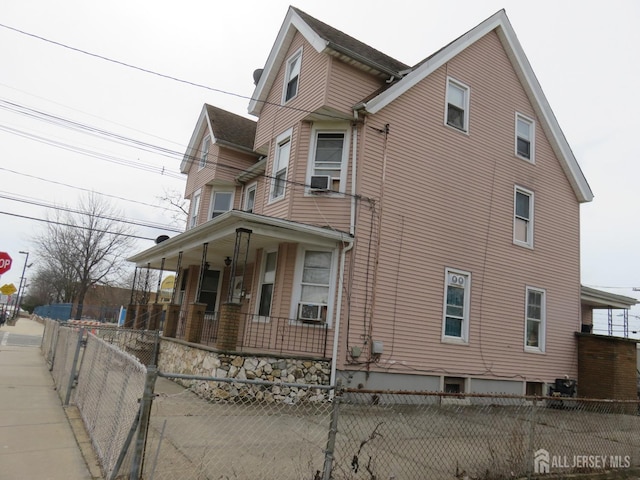 view of side of home with a fenced front yard, covered porch, and cooling unit