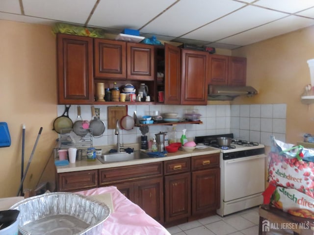 kitchen with backsplash, under cabinet range hood, light countertops, white gas range, and a sink