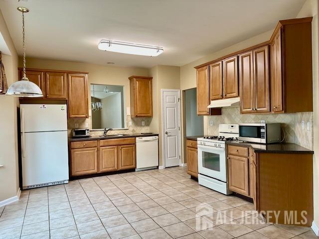 kitchen featuring white appliances, under cabinet range hood, dark countertops, and backsplash