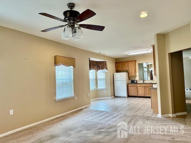 kitchen with freestanding refrigerator, baseboards, light tile patterned floors, light carpet, and a sink