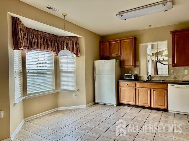 kitchen featuring white appliances, a sink, dark countertops, decorative backsplash, and brown cabinetry