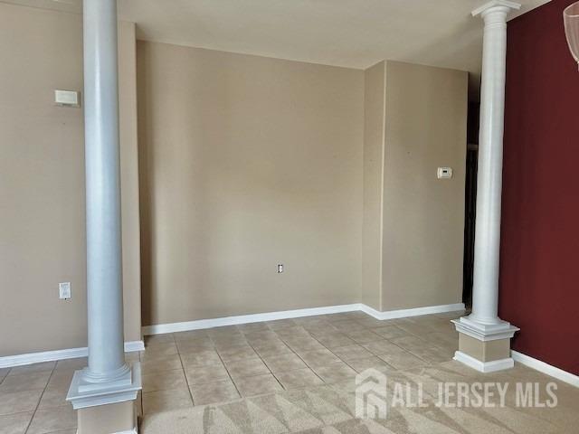 empty room featuring light tile patterned floors, decorative columns, and baseboards
