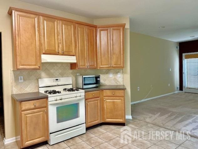 kitchen with white gas range oven, under cabinet range hood, stainless steel microwave, backsplash, and baseboards