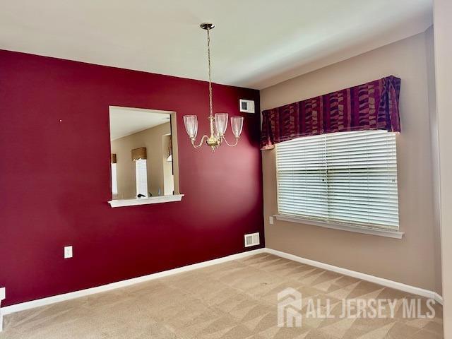 empty room featuring a chandelier, baseboards, and carpet