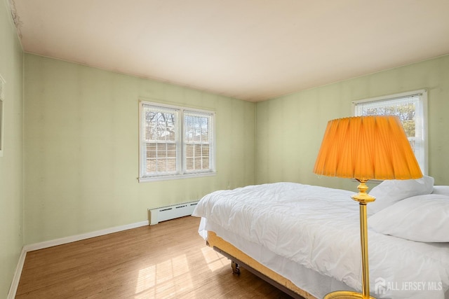 bedroom with a baseboard radiator, multiple windows, baseboards, and wood finished floors