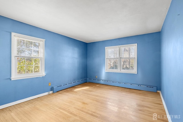 spare room with baseboard heating, light wood-type flooring, and baseboards