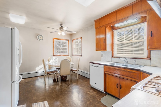 kitchen featuring light countertops, baseboard heating, brown cabinetry, a sink, and white appliances