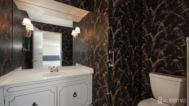 half bathroom with vanity, toilet, and wallpapered walls