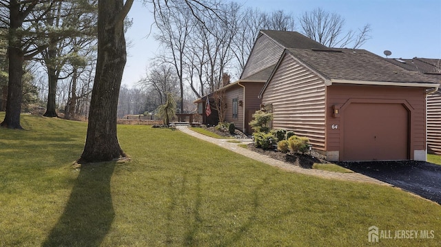 view of home's exterior featuring a yard, a chimney, a shingled roof, a garage, and driveway