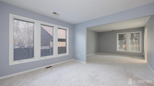 spare room featuring plenty of natural light, baseboards, visible vents, and light colored carpet