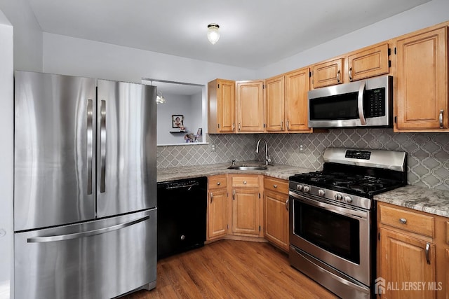 kitchen featuring appliances with stainless steel finishes, tasteful backsplash, sink, light stone countertops, and light hardwood / wood-style flooring